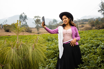 Foto de una feliz y bonita campesina con un sombrero hablando por un teléfono celular en los Andes...