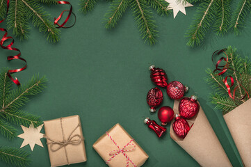 Two paper cone bags with Christmas glass red toys and fir branches and gift boxes on green background. Boxing day concept, DIY gifts.