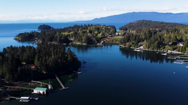 Aerial footage over Madeira Park, Sunshine Coast, British Columbia. Moving towards towards homes with docks stretching into the still water, tilting down to focus on a house by the water