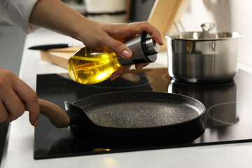 Woman with bottle of oil and frying pan in kitchen, closeup