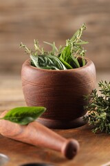 Different fresh herbs in mortar with pestle on wooden table, closeup