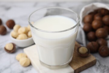 Glass of macadamia milk and nuts on white marble table, closeup