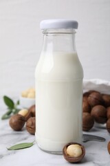 Glass bottle with macadamia milk and nuts on white table, closeup