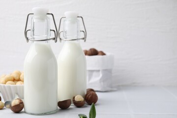 Bottles of macadamia milk and nuts on white tiled table. Space for text
