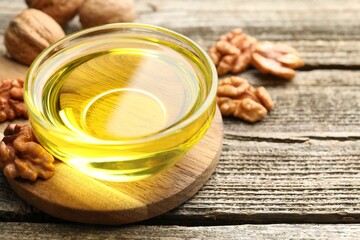 Cooking oil in bowl and walnuts on wooden table, closeup. Space for text