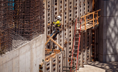 An iron worker on a metal wall with rebar nearby at a construction site