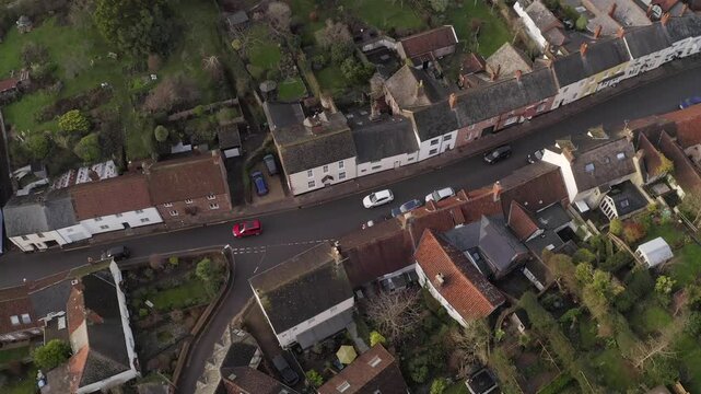 Charming aerial view showcasing traditional British village Dunster in Somerset. The scene includes a winding street, historic homes, and lush gardens, capturing the essence of countryside living.