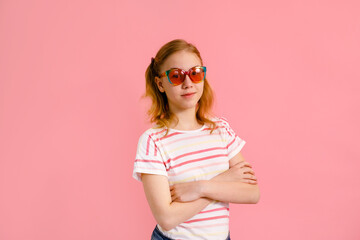 Emotional blonde teen girl in sparkle sunglasses and yellow t-shirt laughing to camera on pink background