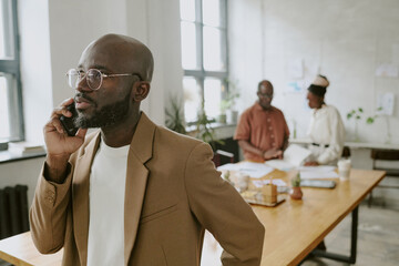 African American worker speaking on phone while his coworkers discussing report in background