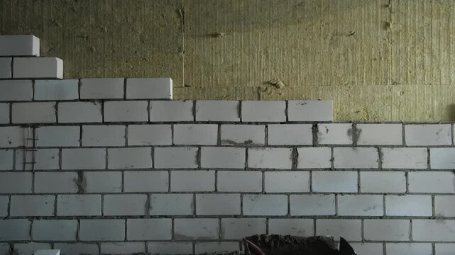 Construction works laying bricks blocks creating walls in building. Rough finishing build works. Construction site with materials in room of apartment. Insulation strengthening of walls from inside.
