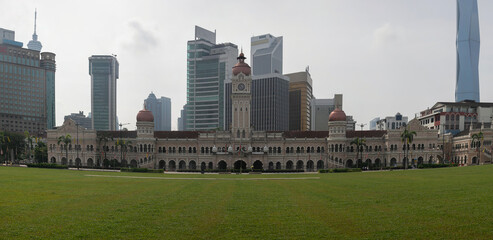 Merdeka Square in Kuala Lumpur: glued panorama with high resolution. Old colonial-style buildings on a huge green lawn in the bustling Asian metropolis. Behind downtown with lots of skyscrapers