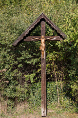 Wooden crucifix in the forest: A weathered wooden cross stands alone in the middle of a green forest.