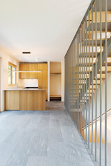 Front view of a modern wooden kitchen with induction cooktop. Above the island is a hanging chandelier and spotlights. The steps of the staircase can be seen to the right. None inside