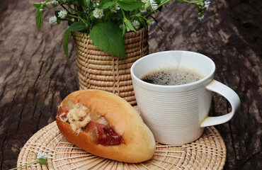 Hot black coffee, bread Stuffed and arranged on a holder next to a vase of white wildflowers. On a dark wooden table

