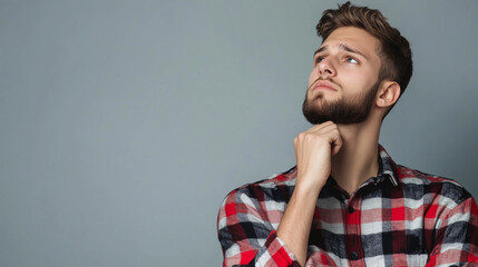 A close-up portrait of a young man in a flannel plaid shirt, his face tense with serious thought, reflecting on his future as he stands against a simple background with copy space.