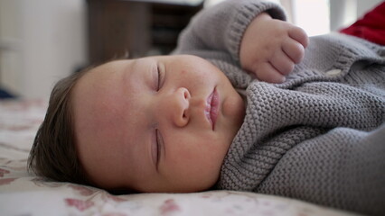 Baby peacefully sleeping on a bed, wearing a knitted sweater, depicting a calm and cozy moment of rest in a warm and nurturing home environment, emphasizing tranquility