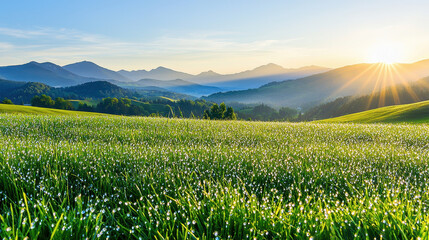 Vibrant sunrise over a dew-covered green meadow with distant mountains and rolling hills illuminated by warm sunlight