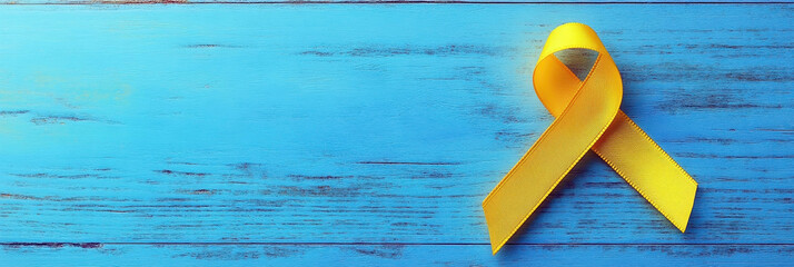 Yellow ribbon on a blue wooden background. Horizontal banner. Free space for text. Childhood Cancer Day. Treatment of sick children concept