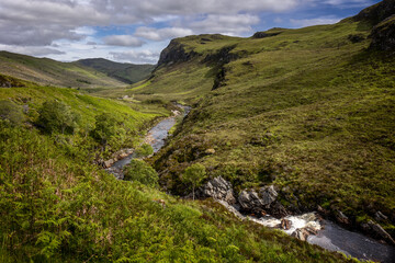 Obraz premium Typical Scottish landscape with hills, rocks, a cloudy blue sky and the many rivers and lochs in the Scottish highlands.