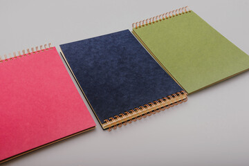 Fototapeta premium Stack of three colourful craft paper spiral binding photo albums in blue, green, and magenta. Ideal for DIY scrapbooking, memory keeping, and creative photo displays in vibrant styles.