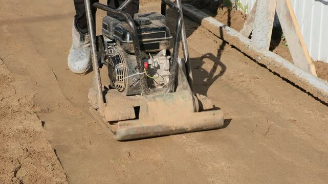 Worker operating a vibrating soil compactor used to compact soil in preparation for paving stones. Construction and renovation.