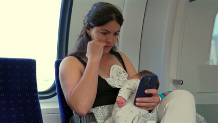 Mother focused on phone while holding baby on lap during a train journey, balance of modern...