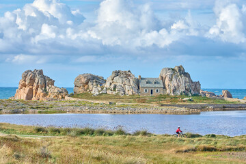 nice senior woman cycling with her electric mountain bike at the rocky rose granite coast of Le Gouffre de Plougrescant, Brittany, France © Uwe