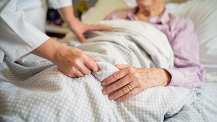 A close-up image of a caregiver gently adjusting the blanket for an elderly patient in a hospital bed. The image conveys a sense of comfort, compassion, and care.