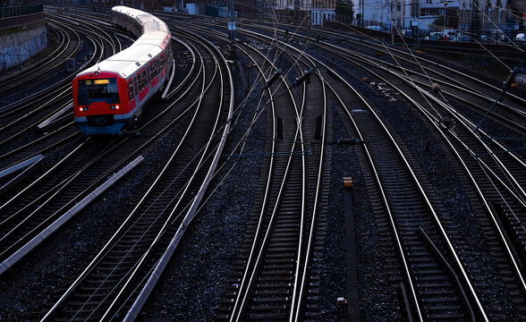 Suburban train on parallel curved railway tracks in Hamburg near main station in morning twilight. Modern red passenger train arriving in german harbor metropole. Public transport system panorama.