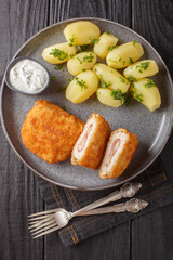 Classic cordon bleu with new potatoes and cream sauce close-up on a plate on a table. Vertical top view from above
