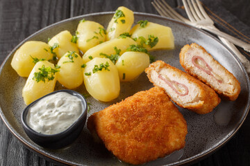 Homemade Breaded Chicken Cordon Bleu with Cheese and Ham served with new potatoes and cream sauce closeup on the plate on the table. Horizontal