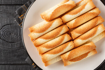 Sweet Russian cigarettes are tender tubes baked to a crispy golden crust close-up in a plate on the table. Horizontal top view from above