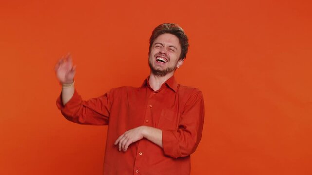 Happy Caucasian young man laughing out loud after hearing ridiculous anecdote, reaction on funny joke, feeling carefree amused. Positive people. Handsome guy isolated on studio orange background
