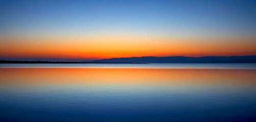 Fototapeta premium A serene sunset over a calm lake, with mountains in the distance and a clear sky