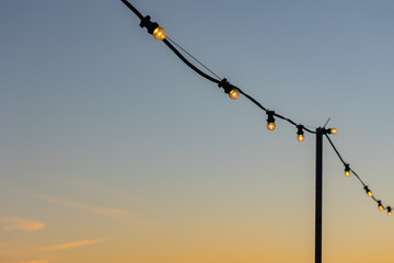 Fairy lights with illuminated light bulbs. Clear sky, sunset, summer.