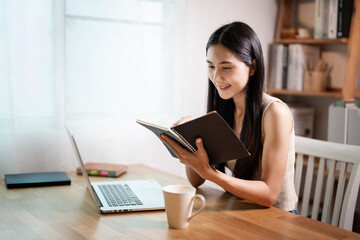 Fototapeta premium Creative young woman reading book and working on laptop in her studio