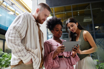 Medium shot of three business people from different ethnic backgrounds collaboratively using digital tablet looking at screen while working in modern office center