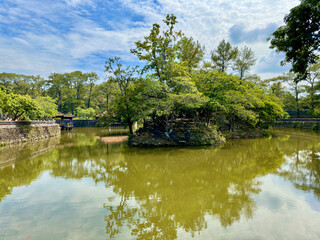 Fototapeta premium A green lake with a small island in the middle with many trees against a blue sky
