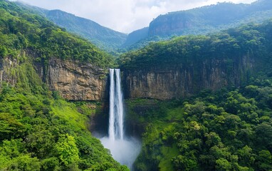 Fototapeta premium A breathtaking waterfall cascades down a rocky cliff, surrounded by lush greenery and majestic mountains under a blue sky.