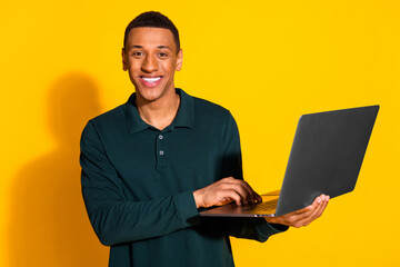 Photo portrait of attractive young man hold netbook dressed stylish green clothes isolated on yellow color background