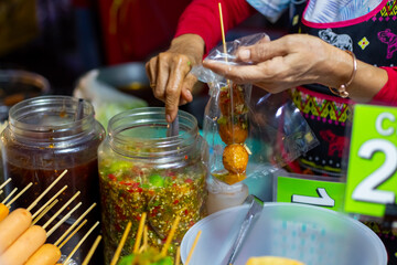Street food. A female vendor pours hot sauce over fried meatballs at a night food market