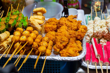 Street food. Fried chicken pieces in batter and meatballs on skewers at a night food market