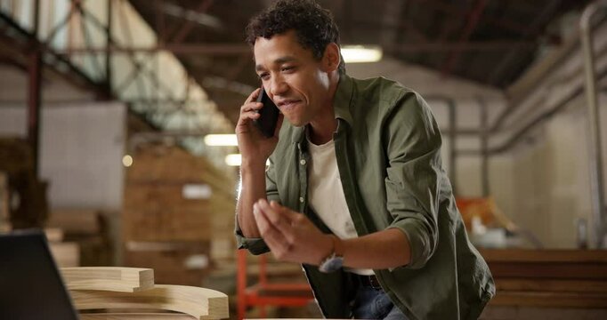 Man, call and factory with carpenter ordering supplies for inventory or restock with stress from supplier. Preparation, warehouse and conversation on cellphone with laptop for equipment order.