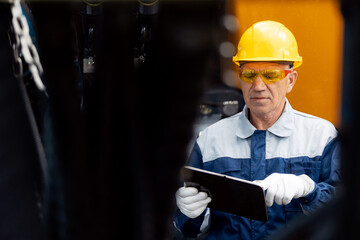 Engineer worker uses computer tablet to configure equipment. Service diagnostics and repair of hydraulic systems and hoses for industrial truck