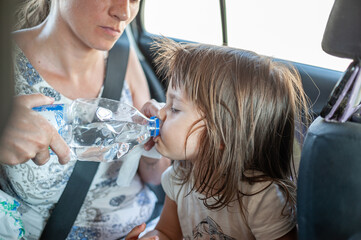 The little girl is drinking the water inside a car