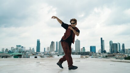 Motion shot of B-boy dance performance by professional street dancer at rooftop with sky scrapper, city view. Attractive asian hipster show energetic footstep. Outdoor sport 2024. Hiphop.
