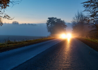 Car headlights on a dark wet road in foggy conditions 
