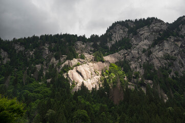 Sunlight breaks through the clouds illuminating a rocky mountain cliff.