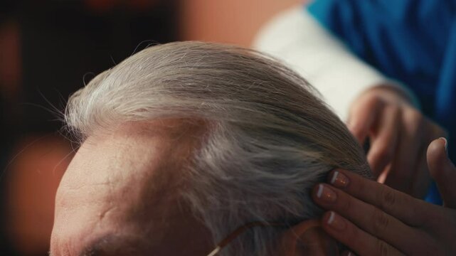 Close-up of caring nursing home worker combing hair of elderly male patient