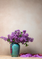 Large bouquet of lush lilac in turkis vase. Purple shades of flowers create delicate image. Background is light, emphasizing freshness and beauty of bouquet. Copy space .